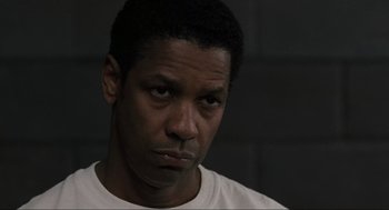 Movie still from “American Gangster” (2007), directed by Ridley Scott – A man in a white t - shirt is looking at the camera; Close Up shot, Over the shoulder angle