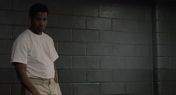 Movie still from “American Gangster” (2007), directed by Ridley Scott – A man standing in front of a brick wall with his hands in his pockets; Medium shot, Low angle