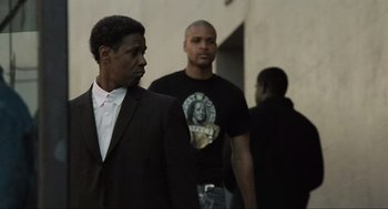 Movie still from “American Gangster” (2007), directed by Ridley Scott – A man in a suit standing next to two other men; Medium shot, Over the shoulder angle