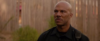 Movie still from “The Hate U Give” (2018), directed by George Tillman Jr. – A bald man in a black shirt is looking to his left; Close Up shot, Over the shoulder angle