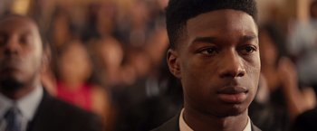 Movie still from “The Hate U Give” (2018), directed by George Tillman Jr. – A young man's face in front of a crowd of onlookers; Close Up shot, Over the shoulder angle