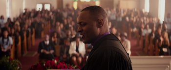 Movie still from “The Hate U Give” (2018), directed by George Tillman Jr. – A man in a robe is standing in front of a group of people; Close Up shot, Over the shoulder angle
