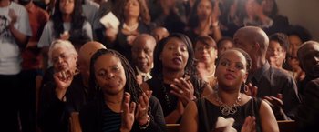 Movie still from “The Hate U Give” (2018), directed by George Tillman Jr. – A group of people sitting in a room clapping; Close Up shot, High angle
