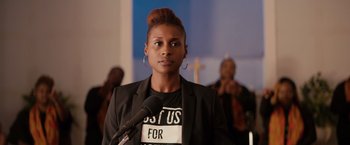 Movie still from “The Hate U Give” (2018), directed by George Tillman Jr. – A woman is speaking into a microphone in front of a crowd; Close Up shot, Over the shoulder angle