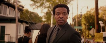Movie still from “The Hate U Give” (2018), directed by George Tillman Jr. – A man wearing a suit and tie standing in front of trees; Close Up shot, Over the shoulder angle