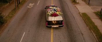 Movie still from “The Hate U Give” (2018), directed by George Tillman Jr. – A car driving down a street with a bunch of flowers in the back; Extreme Wide shot, High angle