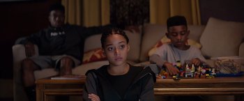 Movie still from “The Hate U Give” (2018), directed by George Tillman Jr. – A young girl sitting in front of a living room couch; Medium shot, Over the shoulder angle