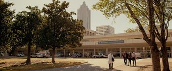 Movie still from “The Hate U Give” (2018), directed by George Tillman Jr. – A person standing in front of a building with cars parked in front of it; Extreme Wide shot, Low angle