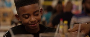 Movie still from “The Hate U Give” (2018), directed by George Tillman Jr. – A young boy sitting at a table with a glass; Close Up shot, Over the shoulder angle