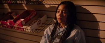 Movie still from “The Hate U Give” (2018), directed by George Tillman Jr. – A woman with long hair is sitting in a store; Medium shot, High angle
