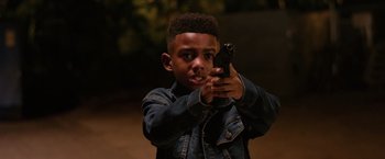 Movie still from “The Hate U Give” (2018), directed by George Tillman Jr. – A young man holding a gun in his hand; Medium shot, High angle