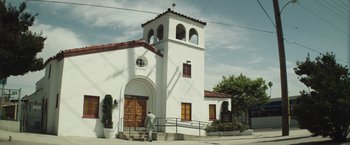 Movie still from “American Sniper” (2014), directed by Clint Eastwood – A man walking in front of a white building; Extreme Wide shot, Low angle
