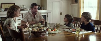 Movie still from “American Sniper” (2014), directed by Clint Eastwood – A man sitting at a dinner table with a child; Medium shot, Over the shoulder angle