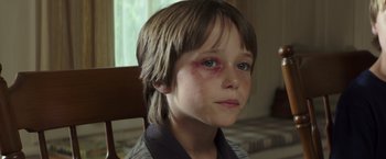 Movie still from “American Sniper” (2014), directed by Clint Eastwood – A young boy with a bruised eye sitting in a chair; Close Up shot, High angle