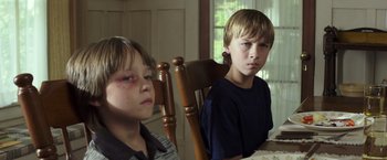Movie still from “American Sniper” (2014), directed by Clint Eastwood – Two young boys sitting at a dining room table; Close Up shot, High angle