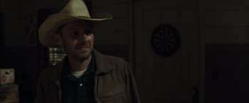 Movie still from “American Sniper” (2014), directed by Clint Eastwood – A man wearing a cowboy hat standing in front of a dartboard; Close Up shot, Over the shoulder angle
