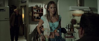 Movie still from “American Sniper” (2014), directed by Clint Eastwood – A woman in a blue shirt holding a can and a bottle; Medium shot, High angle