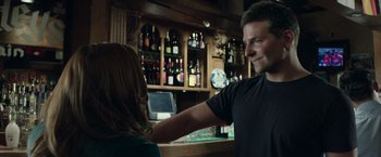Movie still from “American Sniper” (2014), directed by Clint Eastwood – A man and a woman at a bar with bottles of wine behind them; Medium shot, Over the shoulder angle
