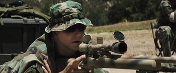 Movie still from “American Sniper” (2014), directed by Clint Eastwood – A man in a camouflage hat is aiming a rifle; Close Up shot, High angle