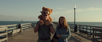 Movie still from “American Sniper” (2014), directed by Clint Eastwood – A man holding a teddy bear next to a woman on a pier; Medium shot, Low angle