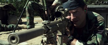 Movie still from “American Sniper” (2014), directed by Clint Eastwood – A man with a rifle looking through the scope of a rifle; Close Up shot, Over the shoulder angle