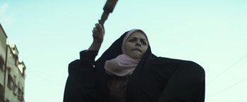 Movie still from “American Sniper” (2014), directed by Clint Eastwood – A woman in a black robe holding a large knife in her hand; Medium shot, Low angle