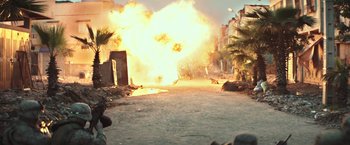 Movie still from “American Sniper” (2014), directed by Clint Eastwood – An explosion is seen coming out of a building; Wide shot, Over the shoulder angle