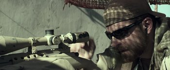 Movie still from “American Sniper” (2014), directed by Clint Eastwood – A man with a rifle aiming at something in the distance; Close Up shot, Over the shoulder angle