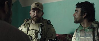 Movie still from “American Sniper” (2014), directed by Clint Eastwood – A man in a military uniform is posing for a picture; Close Up shot, Over the shoulder angle
