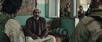 Movie still from “American Sniper” (2014), directed by Clint Eastwood – A man sitting on a couch in front of a mirror; Medium shot, Over the shoulder angle