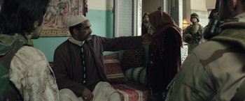 Movie still from “American Sniper” (2014), directed by Clint Eastwood – A man and a woman sitting on a couch in a room; Medium shot, Over the shoulder angle