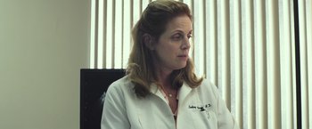 Movie still from “American Sniper” (2014), directed by Clint Eastwood – A woman wearing a white lab coat sitting in front of a window; Close Up shot, Low angle