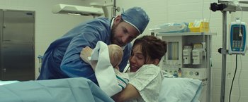 Movie still from “American Sniper” (2014), directed by Clint Eastwood – A man and a woman holding a baby in a hospital bed; Medium shot, Over the shoulder angle