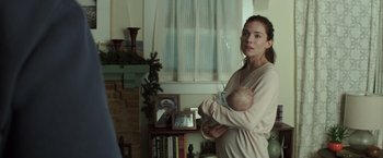 Movie still from “American Sniper” (2014), directed by Clint Eastwood – A woman holding a baby in her arms in a living room; Medium shot, Over the shoulder angle