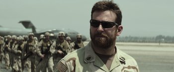 Movie still from “American Sniper” (2014), directed by Clint Eastwood – A man with a beard wearing sunglasses and a military uniform; Close Up shot, Over the shoulder angle