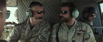 Movie still from “American Sniper” (2014), directed by Clint Eastwood – Two military men are sitting in the back of a helicopter; Close Up shot, Over the shoulder angle