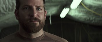 Movie still from “American Sniper” (2014), directed by Clint Eastwood – A person with a beard looking at the camera; Close Up shot, Over the shoulder angle