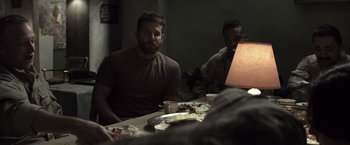 Movie still from “American Sniper” (2014), directed by Clint Eastwood – A group of men sitting at a table with plates of food on it; Medium shot, Over the shoulder angle