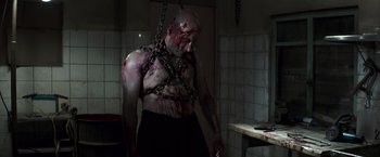 Movie still from “American Sniper” (2014), directed by Clint Eastwood – A man chained to a wall with blood on his face; Medium shot, Low angle