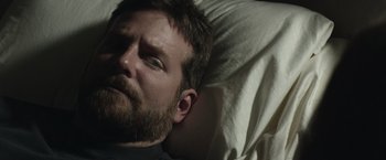 Movie still from “American Sniper” (2014), directed by Clint Eastwood – A bearded man laying in a bed with a white sheet; Close Up shot, High angle