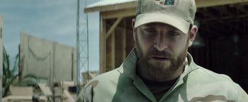 Movie still from “American Sniper” (2014), directed by Clint Eastwood – A person with a beard wearing a hat; Close Up shot, Over the shoulder angle