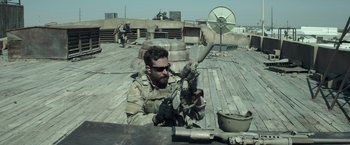 Movie still from “American Sniper” (2014), directed by Clint Eastwood – A man in military fatigues is holding a gun; Medium shot, Over the shoulder angle