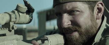 Movie still from “American Sniper” (2014), directed by Clint Eastwood – A man with a beard holding a roll of toilet paper in front of him; Close Up shot, Over the shoulder angle