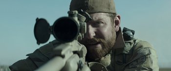Movie still from “American Sniper” (2014), directed by Clint Eastwood – A man with a beard is holding a rifle; Close Up shot, Over the shoulder angle