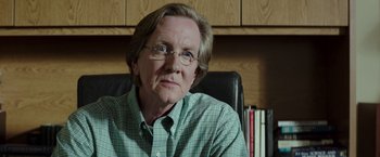 Movie still from “American Sniper” (2014), directed by Clint Eastwood – An older man wearing glasses sitting in a chair; Close Up shot, Over the shoulder angle