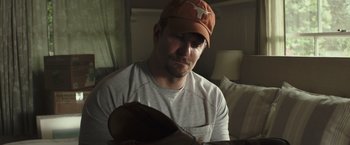 Movie still from “American Sniper” (2014), directed by Clint Eastwood – A man wearing a hat looking down at a guitar; Close Up shot, High angle