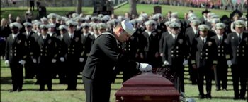 Movie still from “American Sniper” (2014), directed by Clint Eastwood – A man in a navy uniform places his hand on a casket; Wide shot, Over the shoulder angle