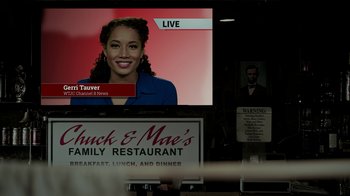 Movie still from “Amityville Uprising” (2022), directed by Thomas J. Churchill – A television screen showing a woman sitting in front of a restaurant sign; Medium shot, Over the shoulder angle