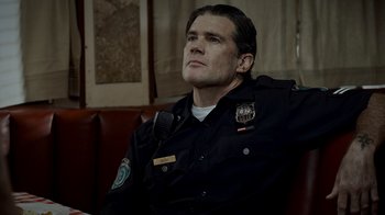 Movie still from “Amityville Uprising” (2022), directed by Thomas J. Churchill – A man in a police uniform sitting on a couch; Close Up shot, Low angle