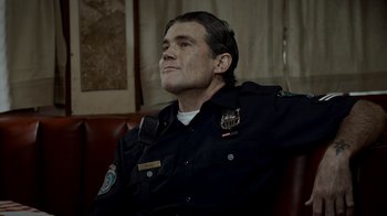 Movie still from “Amityville Uprising” (2022), directed by Thomas J. Churchill – A man in a police uniform sitting on a couch; Close Up shot, Low angle